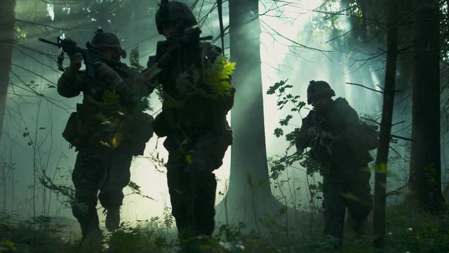 Squad of Five Fully Equipped Soldiers in Camouflage on a Reconnaissance Military Mission, Rifles Ready to Shoot. They're Moving in Formation Through Dense Sunny Forest. 