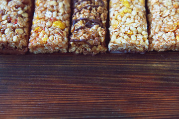Variety of cereal bars with nuts, seeds, dried fruits and chocolate on the wooden table,top view.