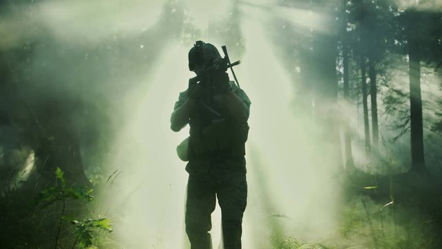 Silhouette of the Fully Equipped Soldier Moving Through Smokey Forest with Rifle Ready To Shoot. Reconnaissance Military Operation. Squad Moving Behind Him. Shot on RED EPIC-W 8K Helium Cinema Camera.