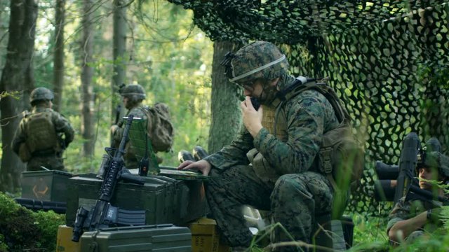 Military Staging Base, Chief Army Engineer Uses Walkie-Talkie Radio and Army Grade Laptop. Squads Resides in Camouflaged Tent While Being on Reconnaissance Operation/ Mission.