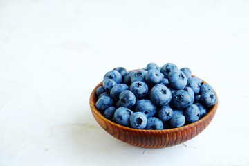 Ripe fresh blueberries in a wooden bowl on white background.