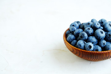 Ripe fresh blueberries in a wooden bowl on white background.