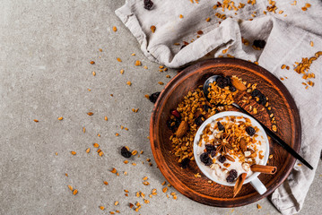 Ideas for an autumn winter breakfast. Spicy yoghurt with granola, dried berries, nuts, almonds, spices (cinnamon, anise), in cup, on plate. Gray background, copy space top view