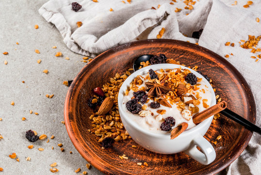 Ideas for an autumn winter breakfast. Spicy yoghurt with granola, dried berries, nuts, almonds, spices (cinnamon, anise), in cup, on plate. Gray background, copy space