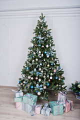 New Year tree with toys and gifts at white room. Happy winter holidays concept.