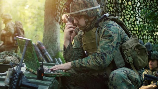Military Staging Base, Chief Army Engineer/ Signalman Uses Walkie-Talkie Radio and Army Grade Laptop. Squads Resides in Camouflaged Tent While Being on Reconnaissance Operation/ Mission. 