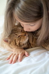 Child playing with cat on bed