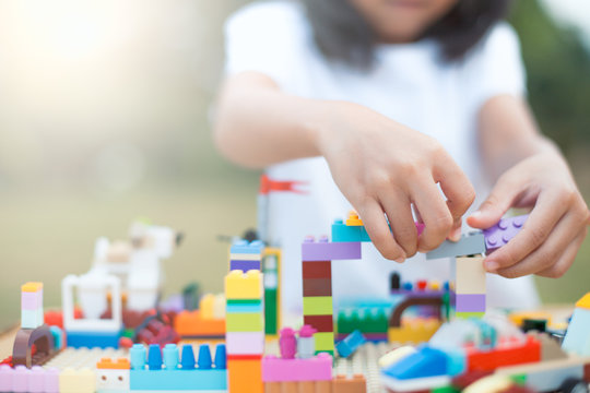 Asian little child girl hand playing with colorful blocks. She is creating and building her toy with fun in good weather outside.