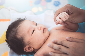 Cute asian newborn baby girl lying down on her bed and looking her mother while mother massaging to her baby after bath