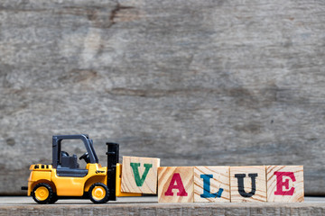 Yellow plastic forklift hold letter V to complete word value on wood background