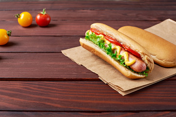Two tasty Hot Dog on craft paper bag with sausages and tomatoes on wooden background. Above view.