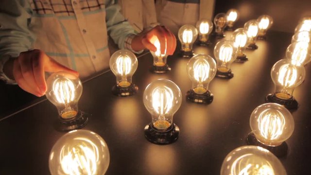 People touch light bulbs displayed on a table.