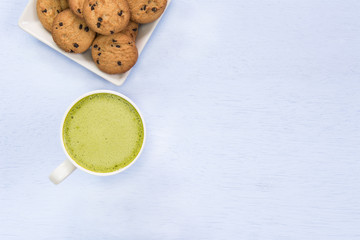 cup of hot matcha latte and chocolate butter cookie on light blue wooden board with copy space, top view.