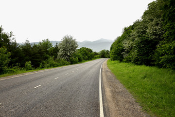 Fototapeta na wymiar Mountain road going through countryside in cloudy day.