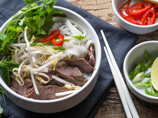Traditional Vietnamese soup- pho in a white bowl with beef and rice noodles, mint and cilantro,...