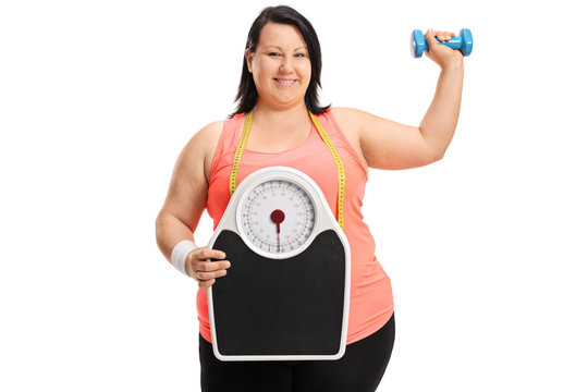 Joyful overweight woman with a weight scale and a small dumbbell