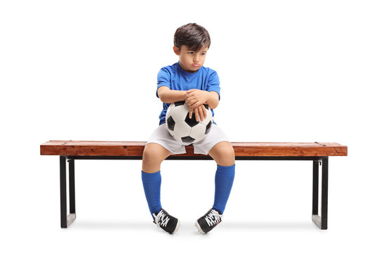 Sad little footballer sitting on a wooden bench