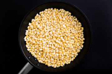 Fresh young corn brewed in water in a frying pan on a black background