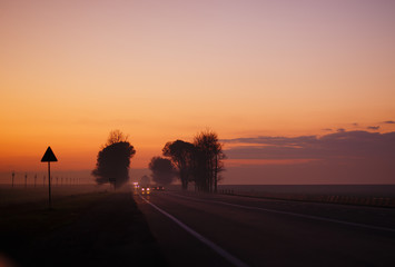 Asphalt road going through the open countryside in colorful sunset light.