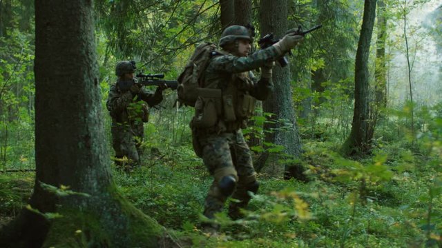Fully Equipped Soldiers Wearing Camouflage Uniform Attacking Enemy, Rifles in Firing Position. Military Operation in Action, Squad Running in Formation Through Dense Forest. 