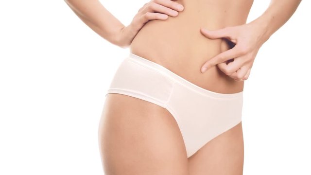 Woman touching her tight stomach. Close up on white background.