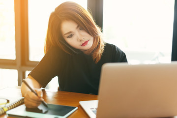 Asian stylish woman designer wear black dress and red lips using smartphone while working with her laptop in selective focus..