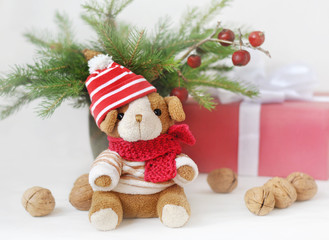 A small  toy dog in a knitted cap, gift boxes, nuts and Christmas spruce branches. Christmas and New Year card. Still life.