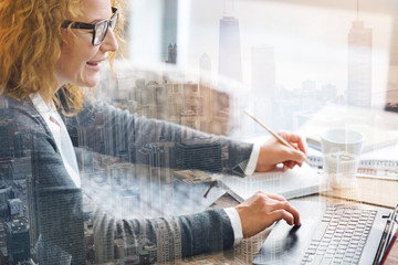 Amusing content. Pleasant fair-haired woman making notes in her notebook while reading an interesting book online and smiling happily
