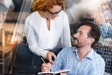 Just curious. Pleasant young woman asking her male colleague about his notes while the man listening to the music and writing in his notebook