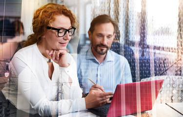 Crucial remarks. Charming red-haired woman sitting next to her male colleague and making some remarks about project presentation while the man taking notes