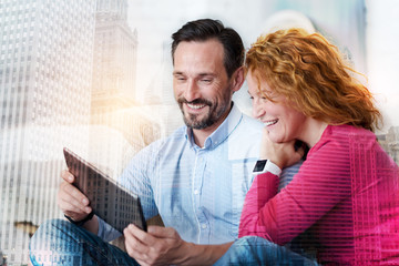 Fototapeta premium Amusing content. Pleasant young man and his charming wife watching funny videos on tablet and laughing