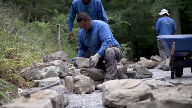 Landscapers and hardscapers gathering large rocks and setting them in place for building a stone wall.