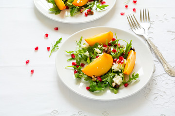Fresh autumn salad with persimmon, arugula, cheese and pomegranate seeds on white table cloth. Space for copy
