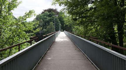 Fussgängerbrücke umrahmt von grünen Bäumen