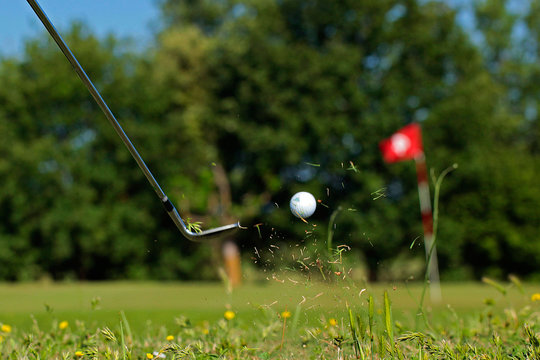 Golfeur frappant une balle avec son club  pour la propulser vers le green et le trou d'arriv&eacute;e.	