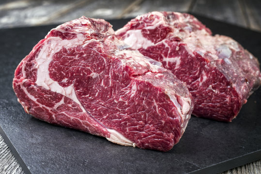 Two Raw dry aged Kobe rib eye steak as close-up on a black board
