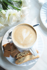 Cup of coffee on the table in cafe with flowers and cookies 