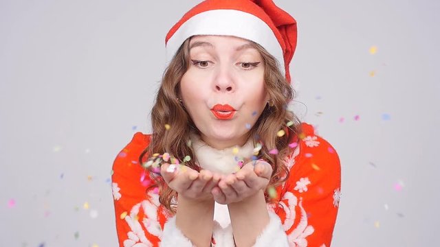 Young woman wearing Santa's hat blowing away confetti