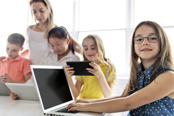 child with technology tablet and laptop computer in classroom teacher on the background