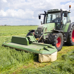 tractor and mower in green meadow in the netherlands on sunny day