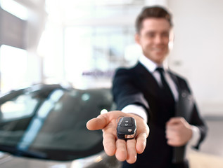 Formal wearing young salesman offers brand new car key. Close up of the key In the foreground. Focus on the key.