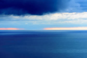 Fototapeta na wymiar Stylized abstract landscape seascape sunset long exposure with clouds under different shades of blue, orange, yellow and red.