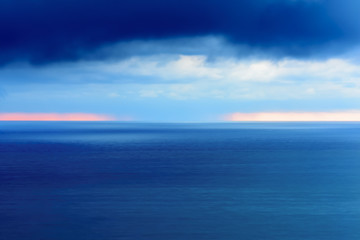 Stylized abstract landscape seascape sunset long exposure with clouds under different shades of blue, orange, yellow and red.