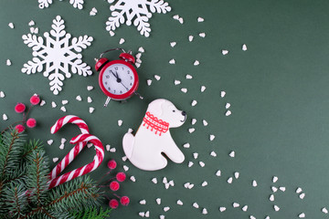 Christmas or new year flat lay cookies in the shape of a dog and snowflakes, fir trees, candy canes and red clock. On green background.