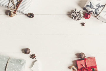 christmas flat lay. presents with ornaments and pine cones anise on white wooden background top view, space for text. stylish wrapped gifts. seasonal greetings card. happy holidays