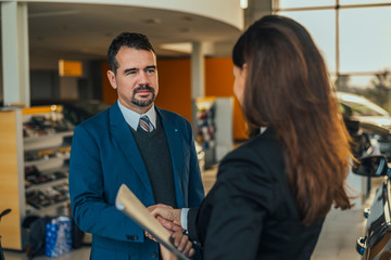 Businessman shaking hands with woman car dealer.