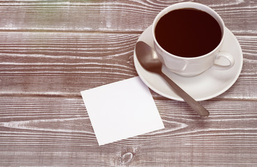a cup of coffee, a spoon, a piece of paper on a wooden table