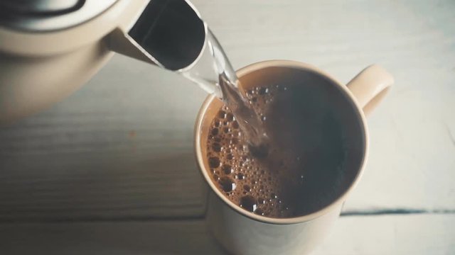 Filling coffee in a ceramic cup with hot water from a kettle