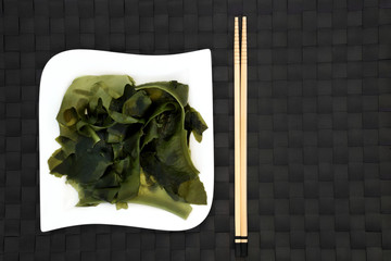 Japanese wakame seaweed food on a square porcelain plate with chopsticks. Has many health benefits and is very high in minerals.