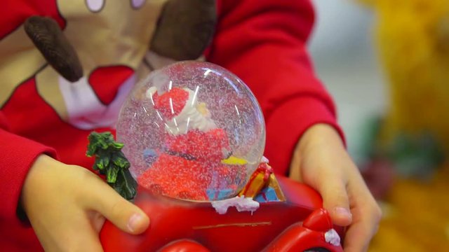 The hands of the little boy are shaking the snow ball in the form of the car. Christmas time.